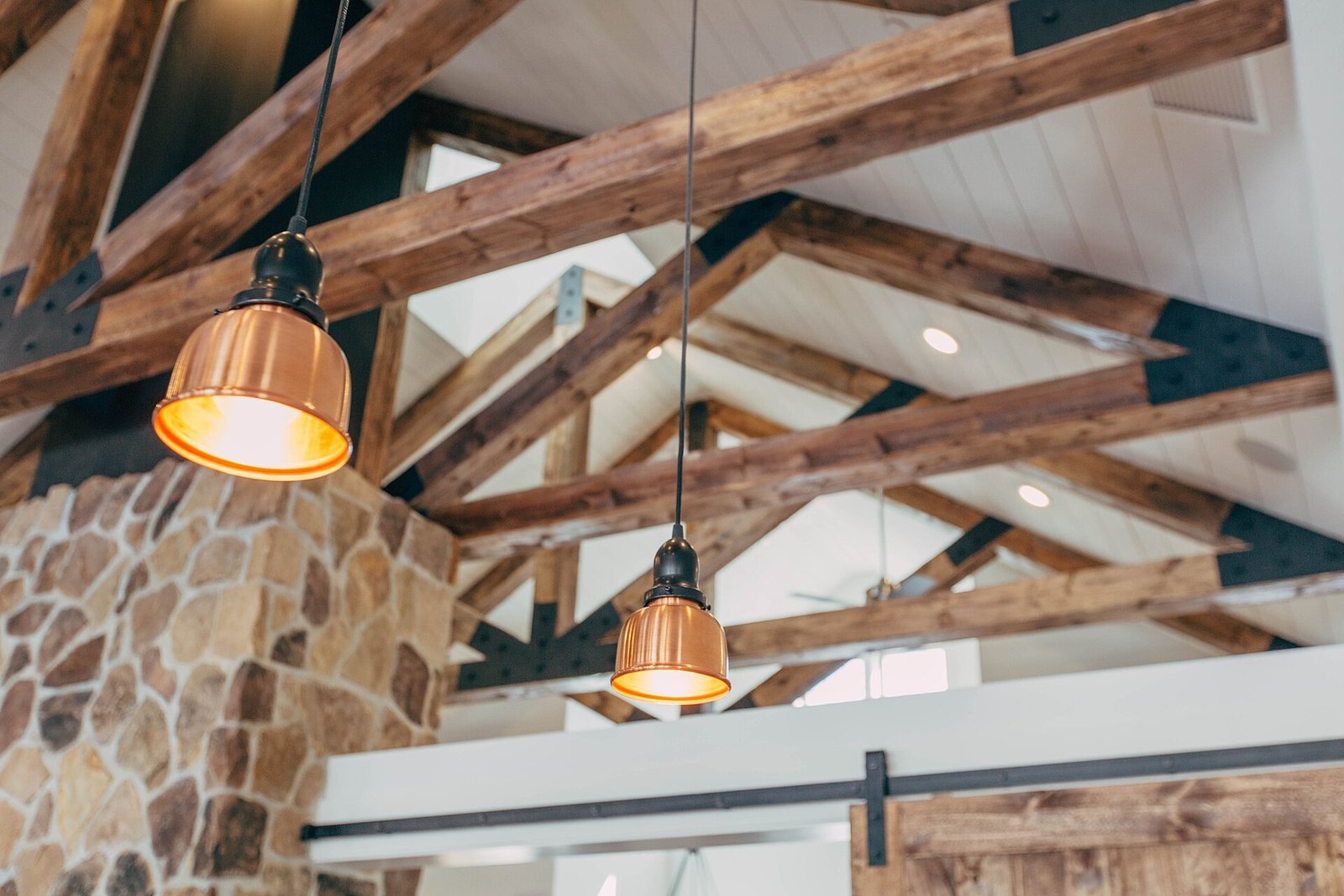 Rustic interior with exposed timber roof beams, a stone wall and copper pendant lamps